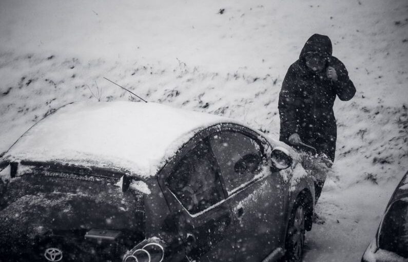 Weather Safety - a man standing next to a car covered in snow