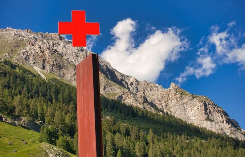 Tree First Aid - brown wooden cross on green grass field near mountain under blue and white cloudy sky during