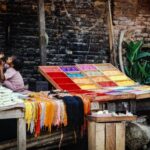 Cultural Practice - a woman sitting on a bench next to a colorful table