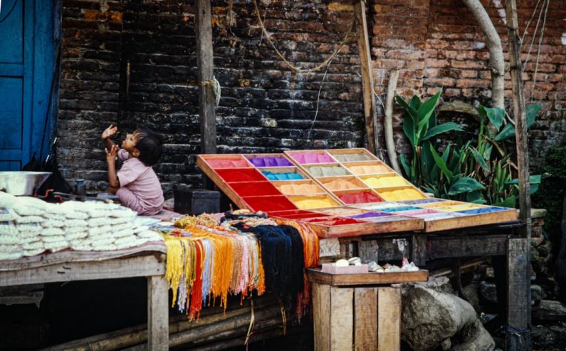 Cultural Practice - a woman sitting on a bench next to a colorful table