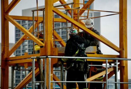 Safety Gear - man in black jacket and helmet climbing orange ladder