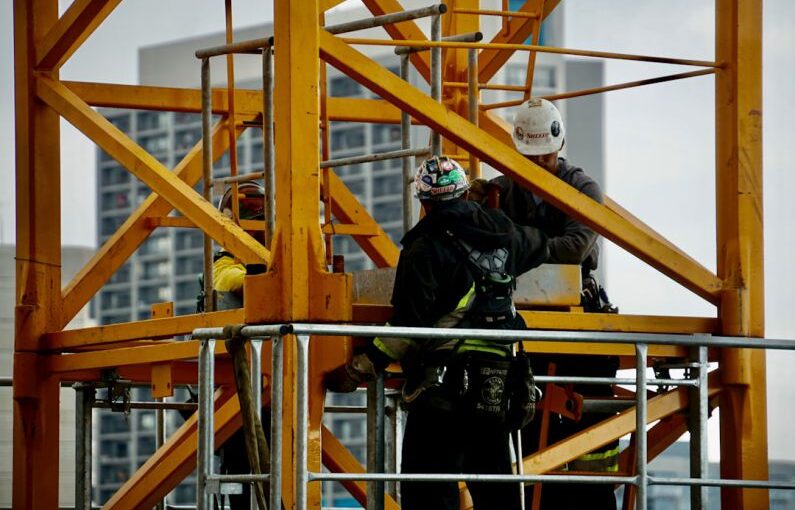 Safety Gear - man in black jacket and helmet climbing orange ladder